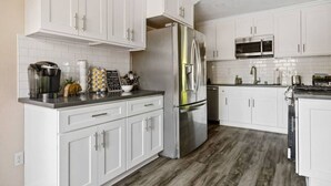A modern kitchen with white cabinets, stainless steel appliances, and a wooden floor. - Charming, cozy and rustic cabin! (Big Bear)