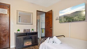 A bedroom with a bed, a fireplace, a mirror, and a painting. - Charming, cozy and rustic cabin! (Big Bear)