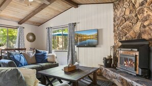 A cozy living room with a stone fireplace, a sofa, a coffee table, and a television. - Charming, cozy and rustic cabin! (Big Bear)