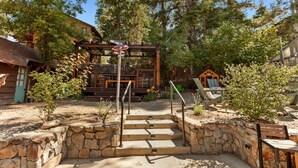 A rustic outdoor area with stone steps leading to a wooden deck, surrounded by trees and a small building. - Pet Friendly With A Hot Tub In Big Bear Lake (Big Bear Lake)