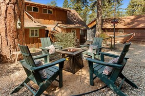 A wooden cabin with a fire pit, outdoor seating, and a hammock.