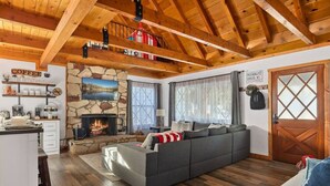A cozy living room with a stone fireplace, a sofa, and a kitchen area with a coffee sign. - Pet Friendly With A Hot Tub In Big Bear Lake (Big Bear Lake)