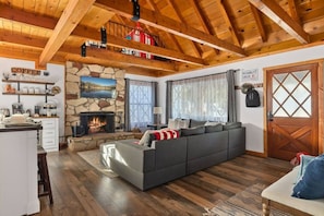A cozy living room with a stone fireplace, a sofa, and a kitchen area with a coffee sign.