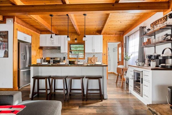 A spacious kitchen with wooden beams, a central island with stools, and a coffee station.