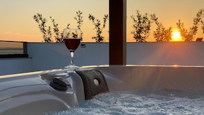 Ett bubbelbad med ett glas rött vin, omgivet av en pool och med utsikt över solnedgången.
