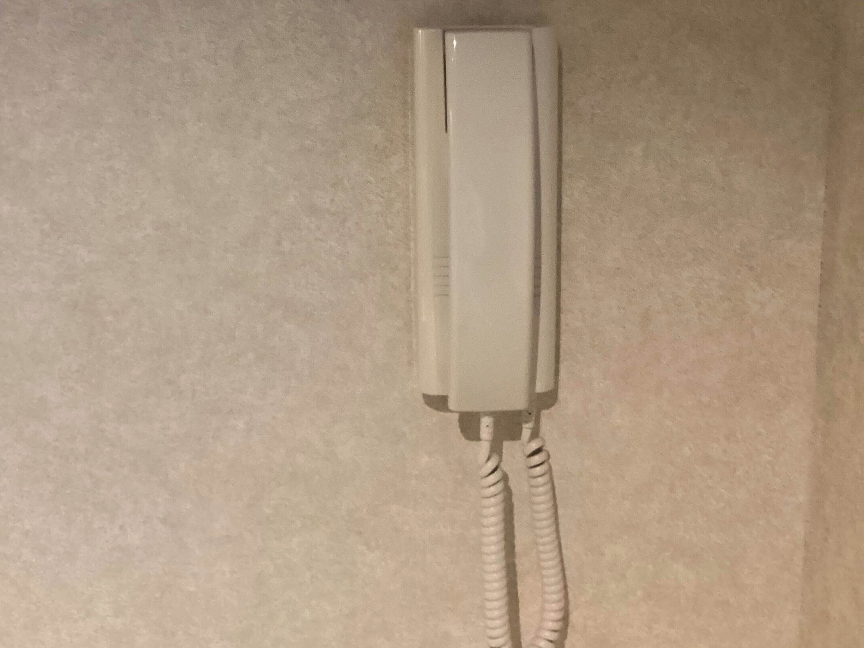 A white telephone handset mounted on a wall.