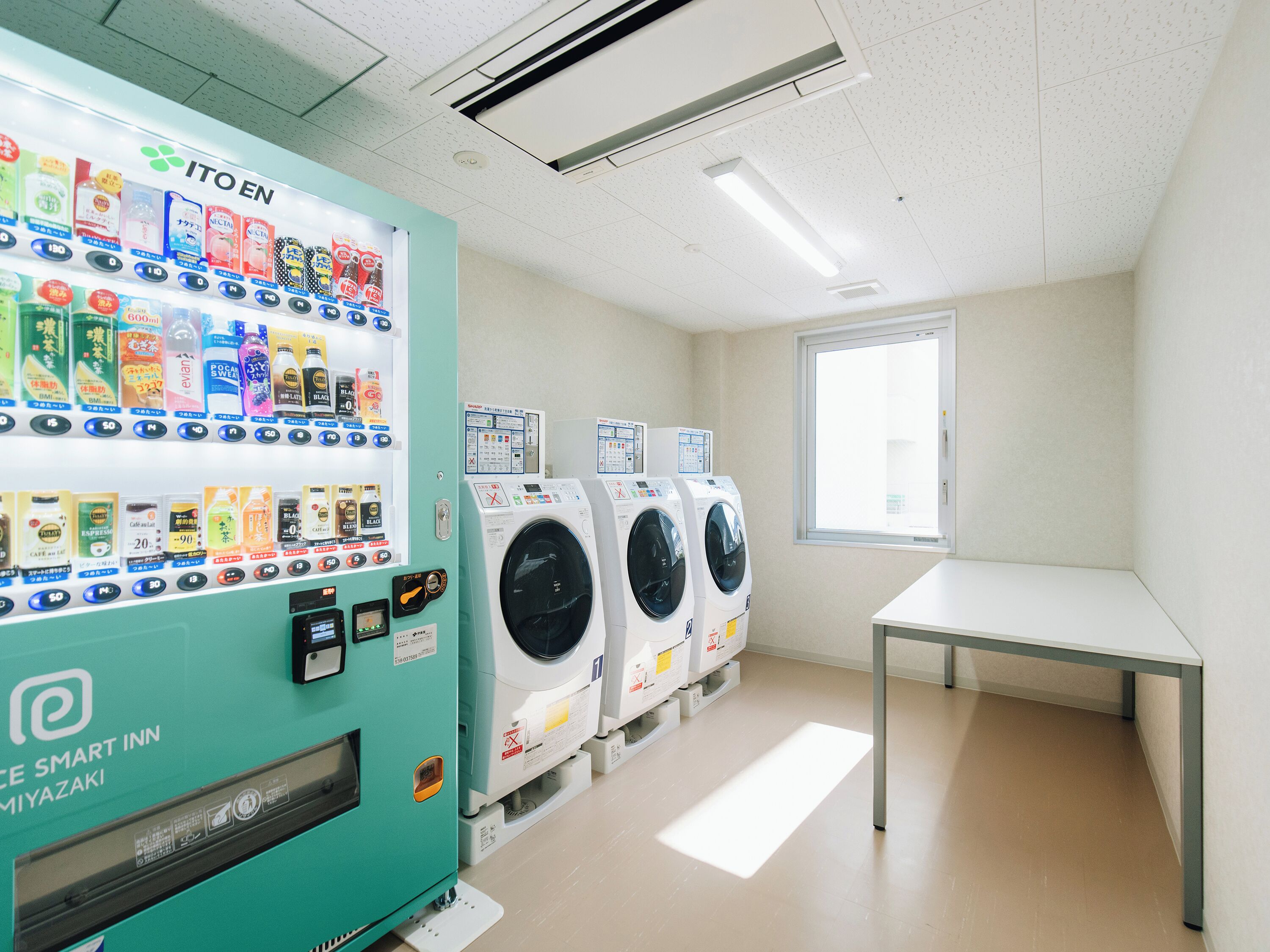 A laundry area with a vending machine, multiple washing machines, and a table.