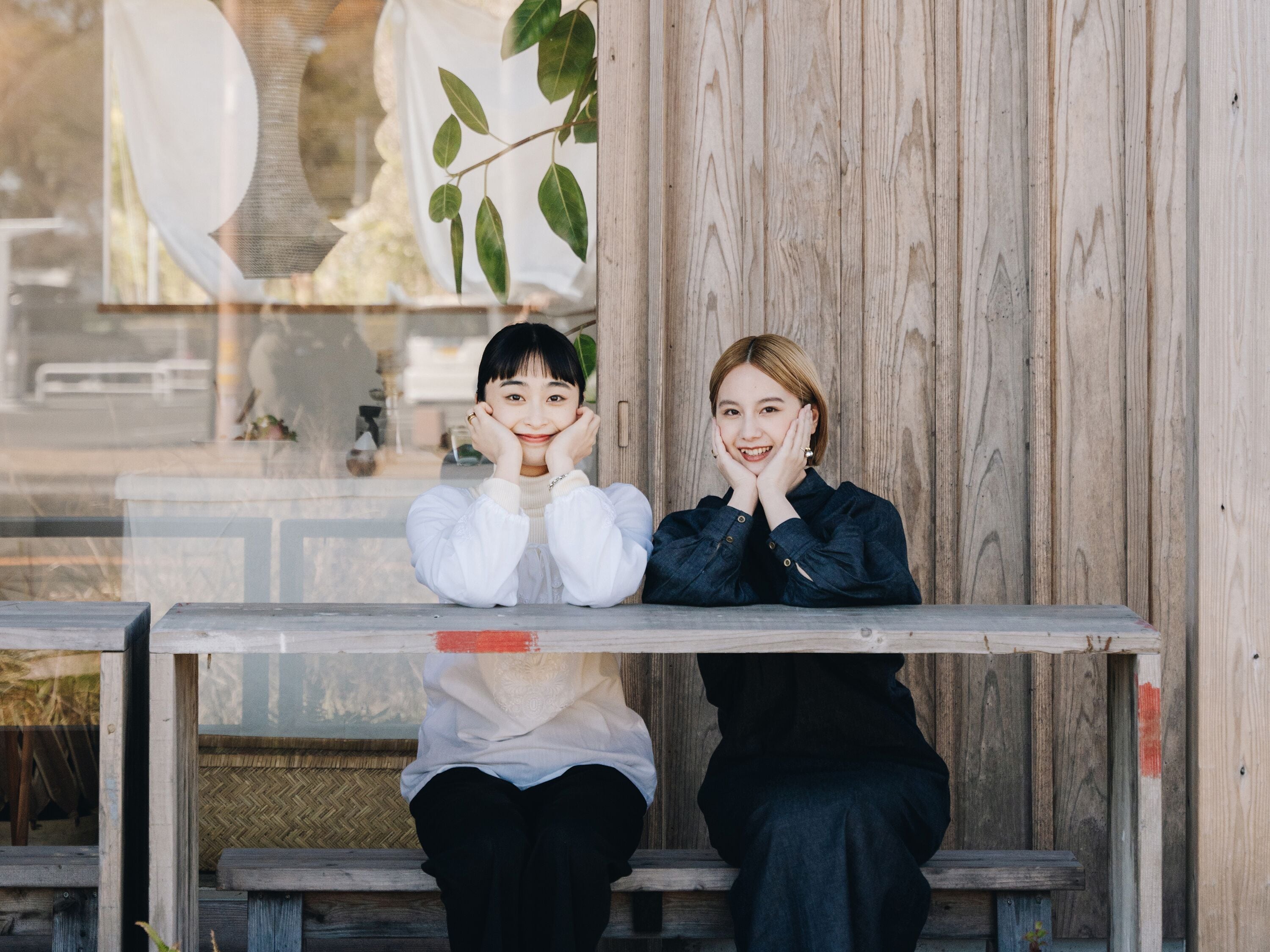 Two people sitting at a wooden bench with a glass table in front of them.