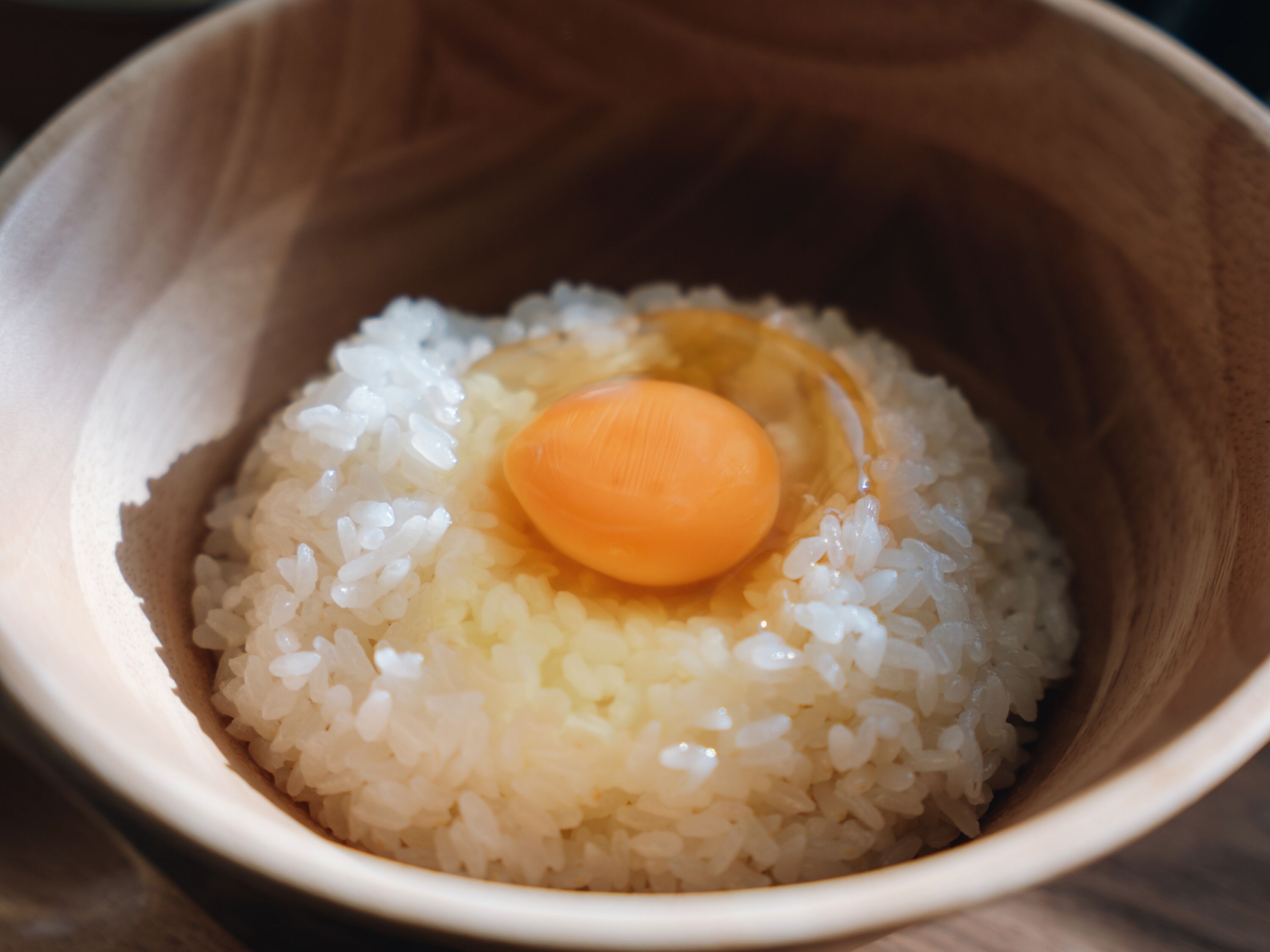 A wooden bowl containing white rice and a single egg yolk.