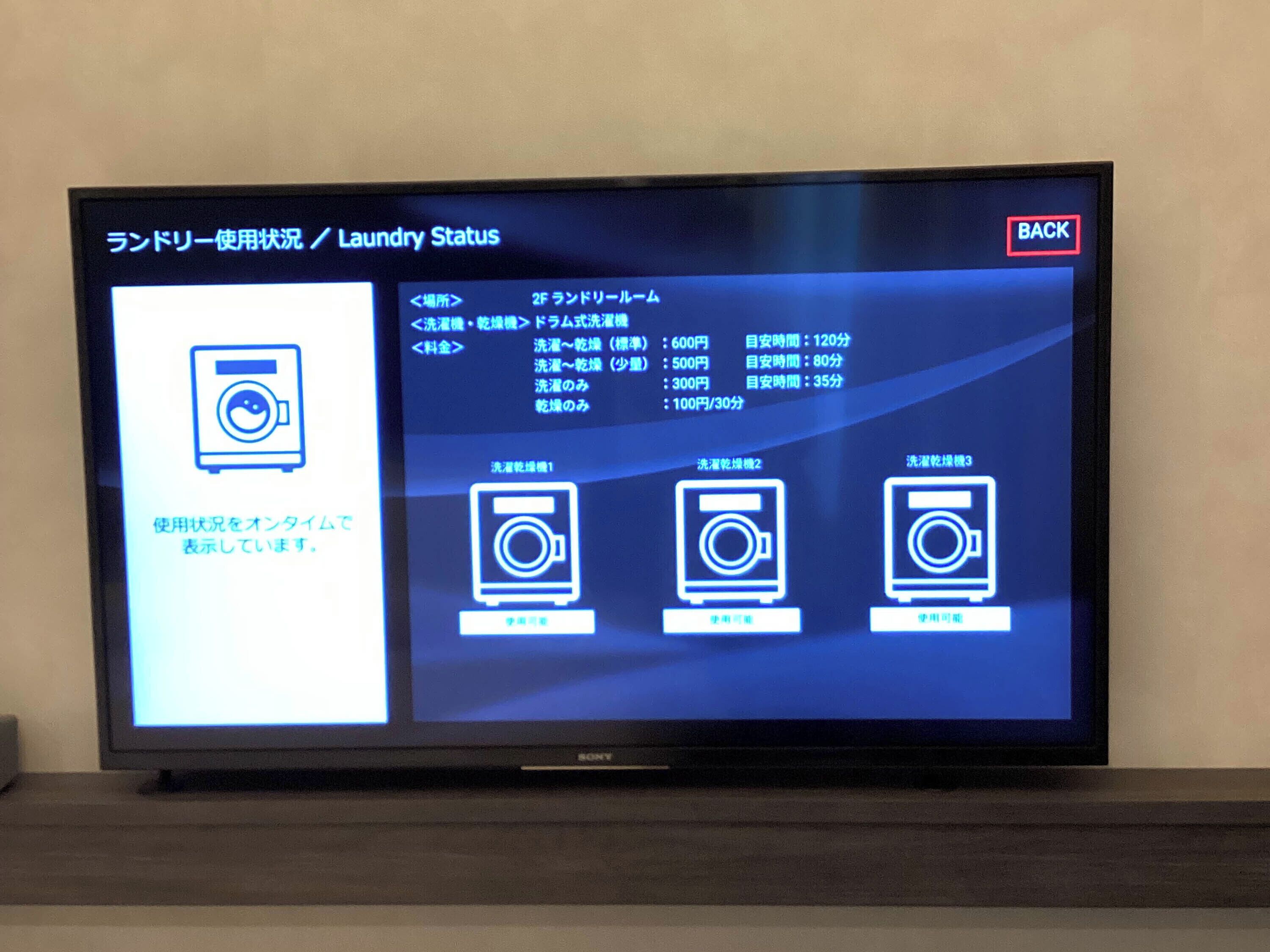 Uma televisão exibindo uma interface de status da lavanderia com opções para diferentes ciclos de lavagem, seus respectivos custos e durações.