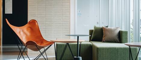 Un área de estar moderna con un sillón de cuero, un sofá verde y dos mesas redondas.