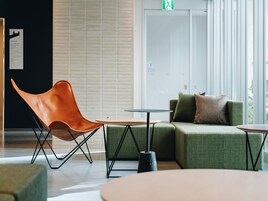 Un área de estar moderna con un sillón de cuero, un sofá verde y dos mesas redondas.