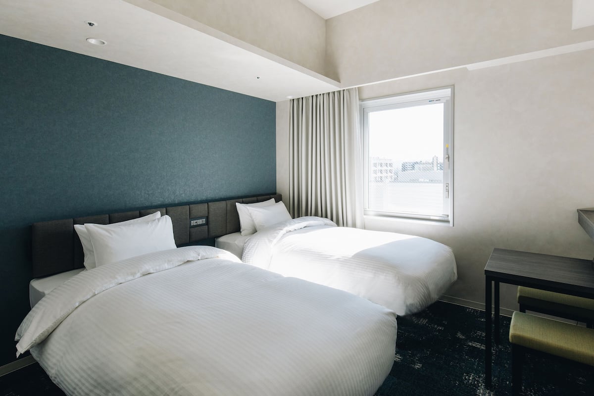 A hotel room with two beds, a desk, and a large window with curtains.