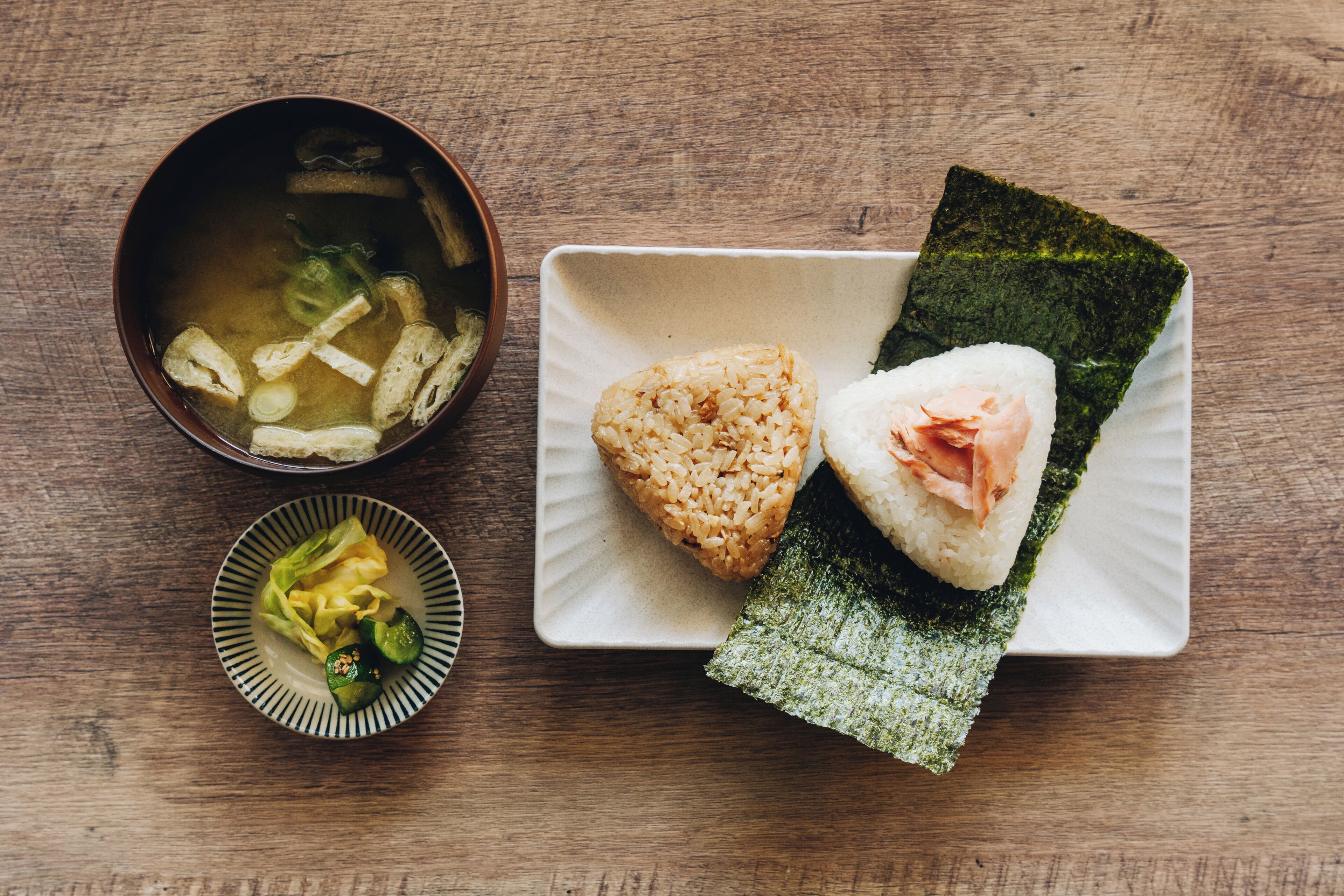 A meal with rice, fish, and vegetables on a plate, and a bowl of soup on a wooden table.