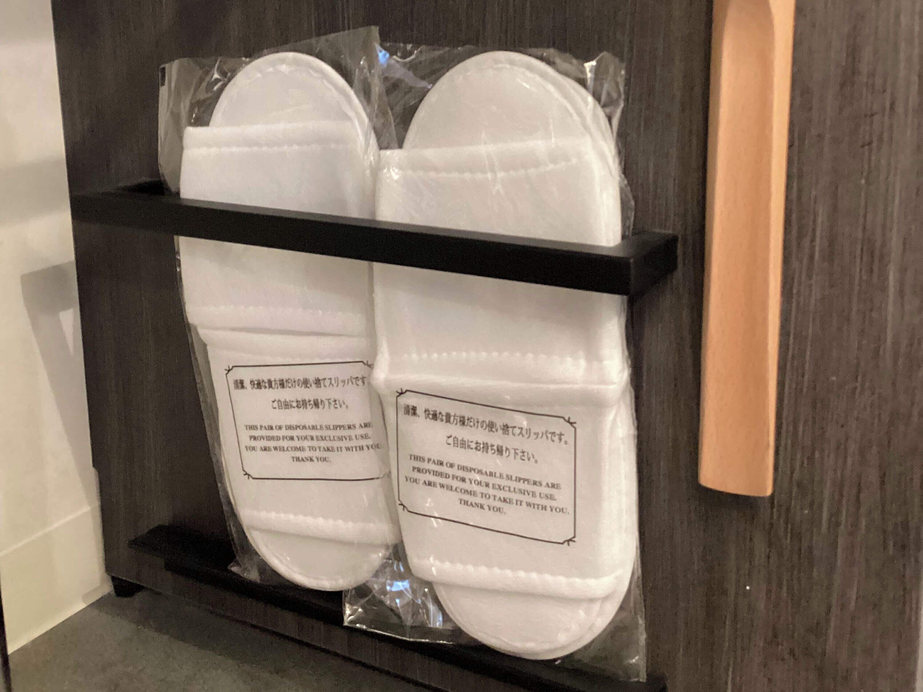 A shelf with four pairs of white disposable slippers in plastic packaging.