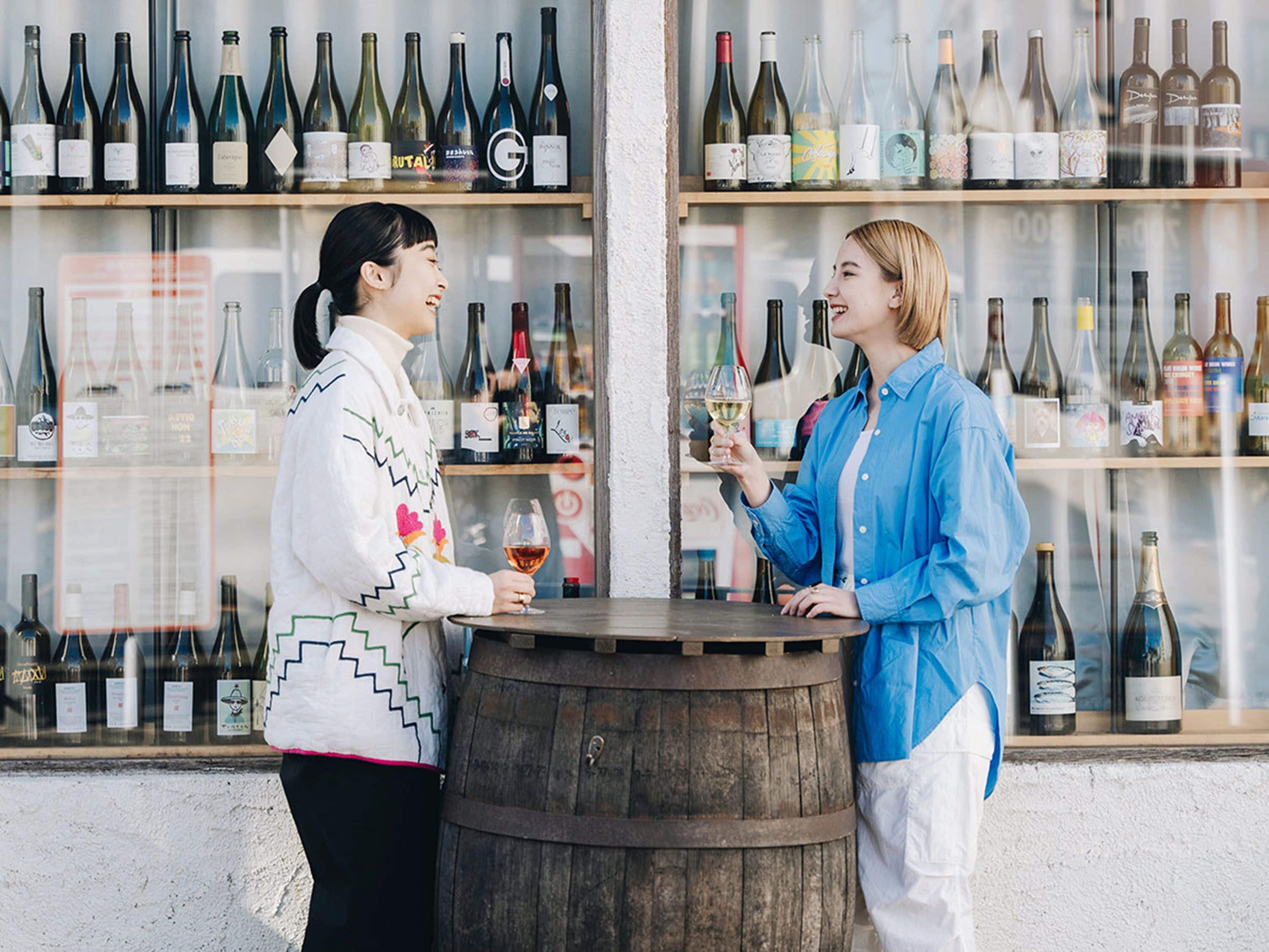 Dos personas de pie en una barra con un barril de madera, rodeadas de estantes llenos de botellas de vino.