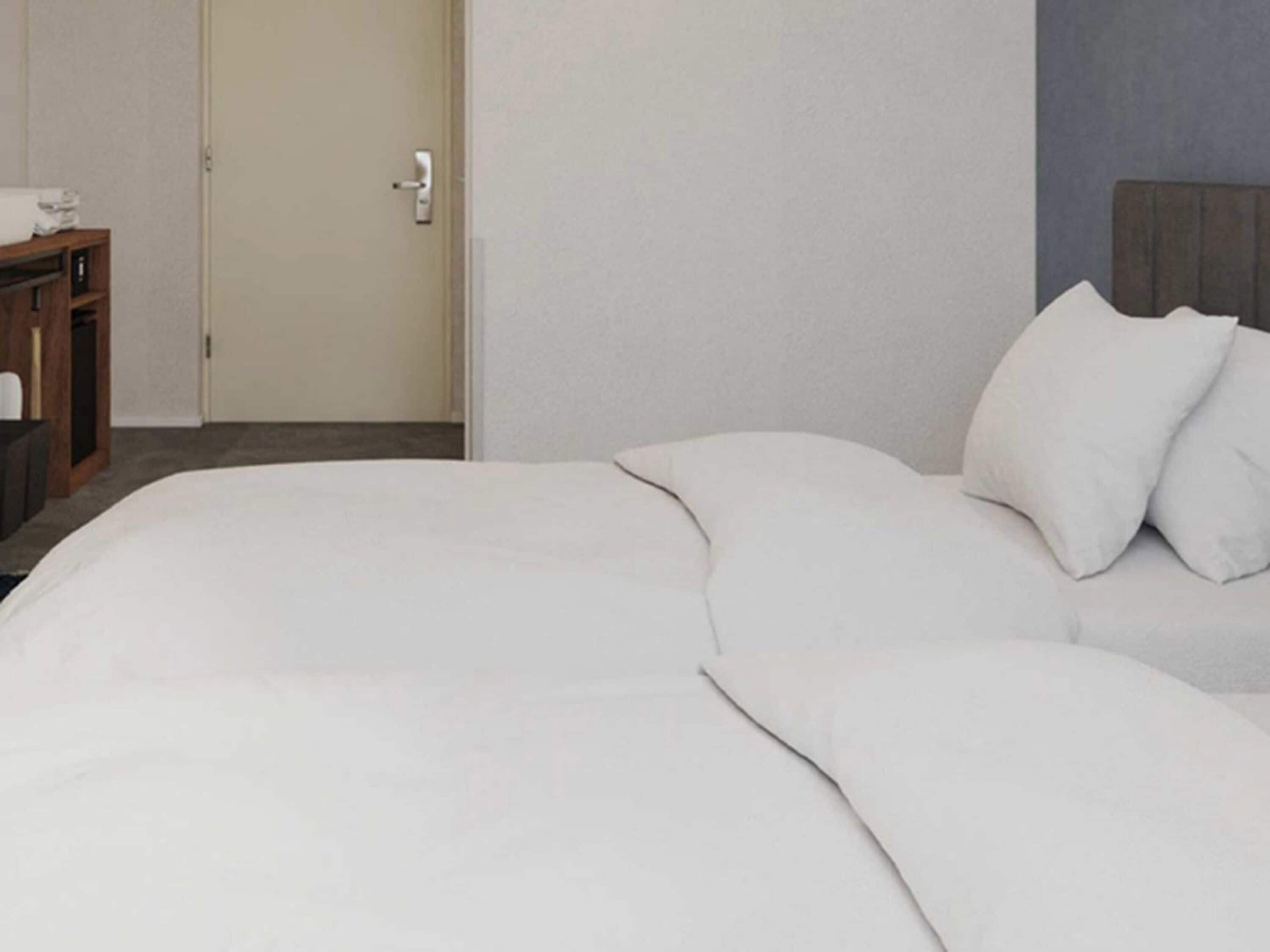 Quarto de hotel com uma cama, uma mesa de cabeceira de madeira e uma porta.