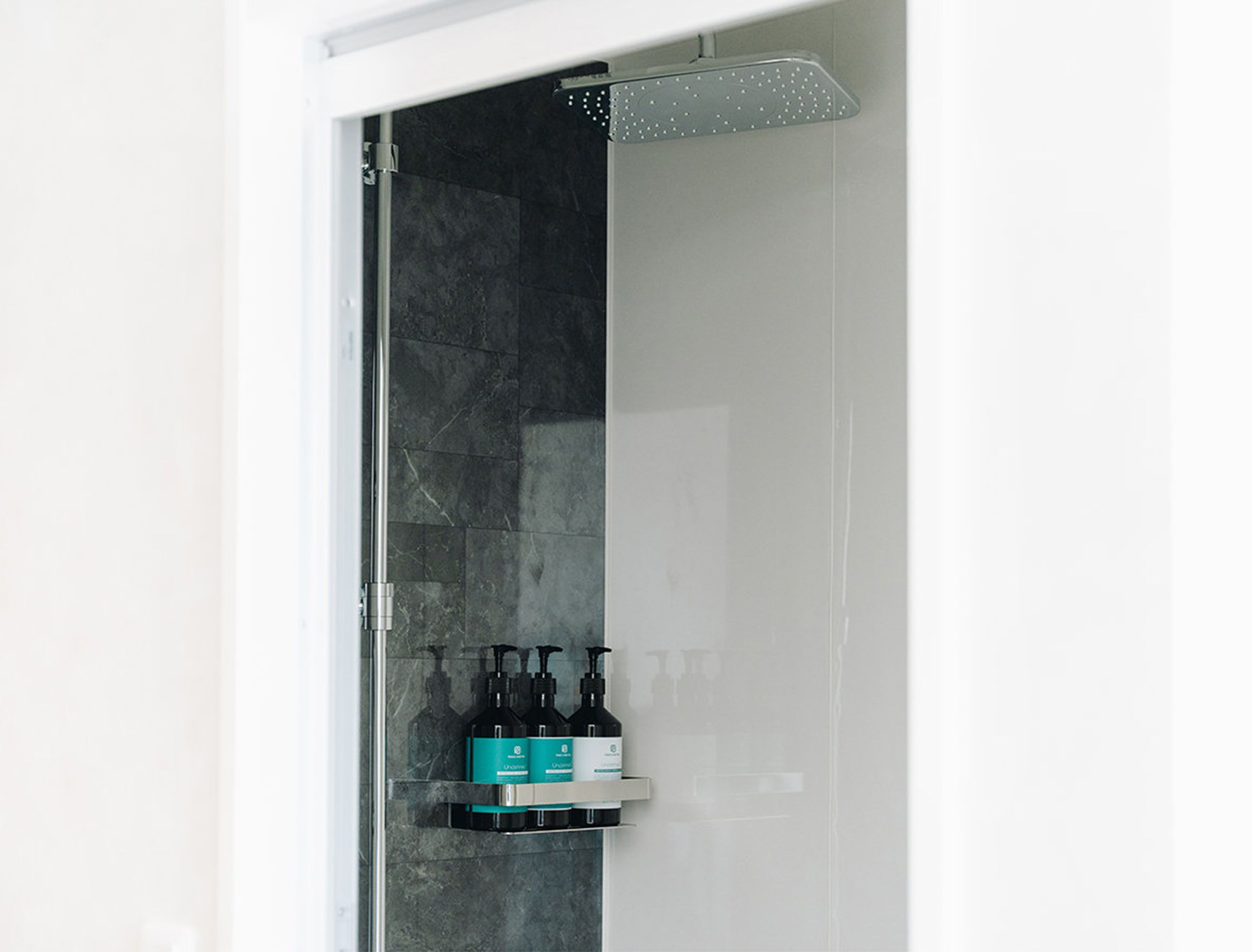 A shower with a glass door, a metal showerhead, and a shelf with toiletries.