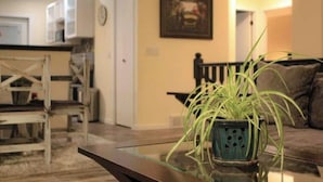 Una sala de estar con una mesa de centro de vidrio, una planta en maceta, un sofá y un cuadro en la pared.