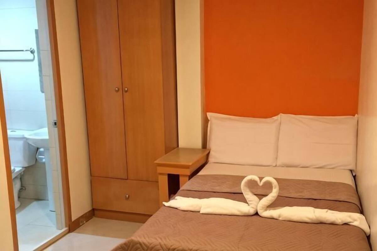 Quarto com uma cama, um guarda-roupa de madeira e um banheiro visível através de uma porta aberta.