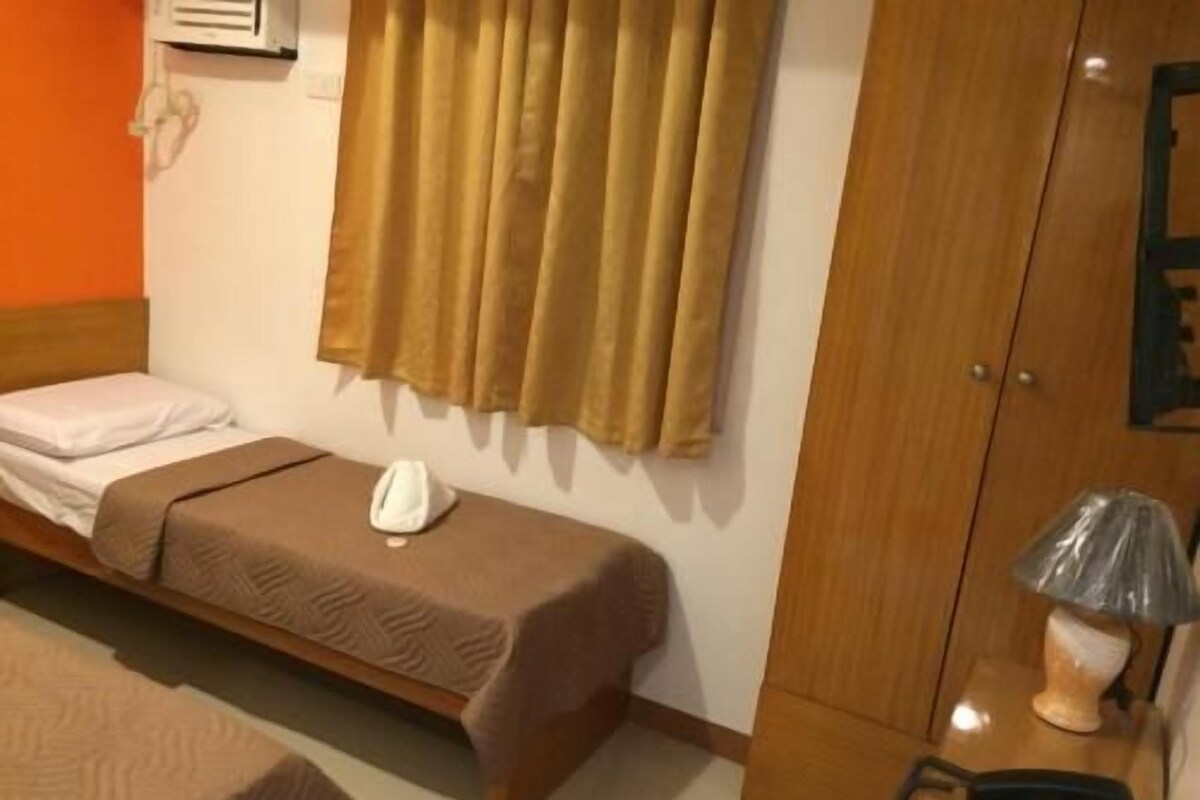 A single bed with a brown bedspread, a bedside table with a lamp, and a wooden wardrobe.