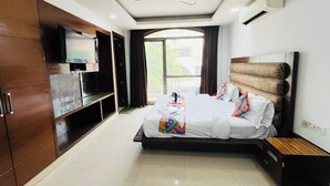 A hotel room with a bed, a TV, a ceiling fan, an air conditioning unit, and a window with curtains. - Roomshala 087 Green High (New Delhi)