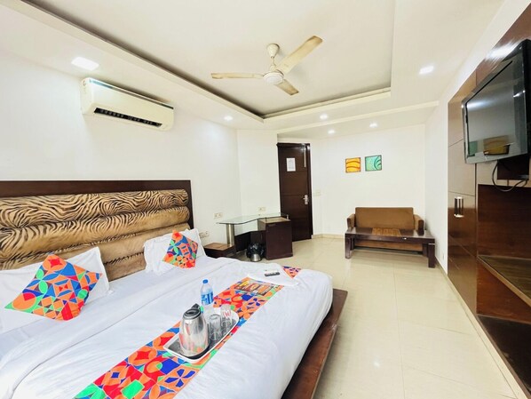 A hotel room with a bed, a TV, a ceiling fan, an air conditioning unit, a desk, a chair, and a door.