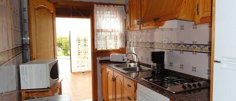A kitchen with wooden cabinets, a stove, a sink, and a microwave.