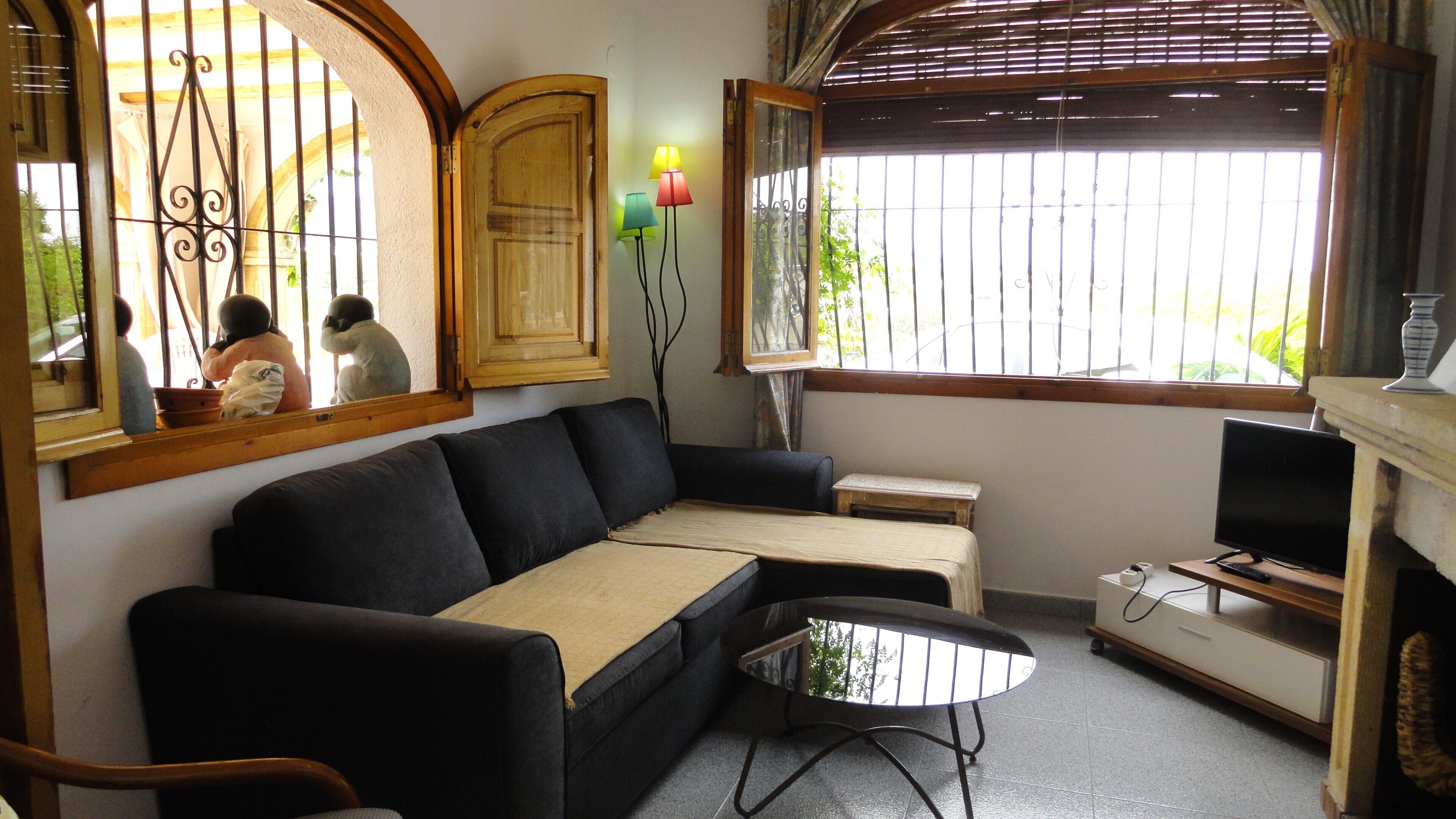 A living room with a sofa, a small table, a television, and a window with bars.