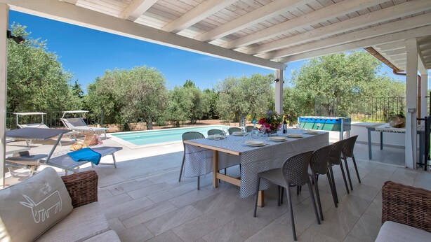 Une terrasse extérieure avec une piscine, des chaises longues, une table à manger et un espace abrité.