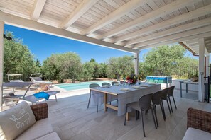 An outdoor patio with a pool, lounge chairs, a dining table, and a covered area. - Villa 'Olivetta' with Private Pool, Wi-Fi, and Air Conditioning (Alghero)