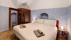 Een slaapkamer met een groot bed, een houten kledingkast en een klein nachtkastje met een lamp.
