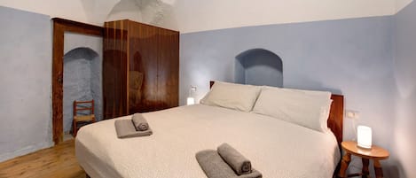 A bedroom with a large bed, wooden wardrobe, and a small bedside table with a lamp.