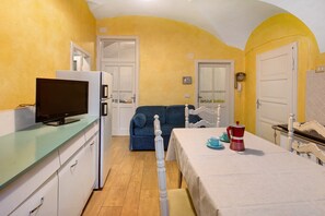 A compact room with a kitchenette, a sofa, a dining table with a red and white coffee pot, and a television on a cabinet.