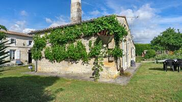Un edificio de piedra con hiedra, una chimenea y un jardín con mesa y sillas.