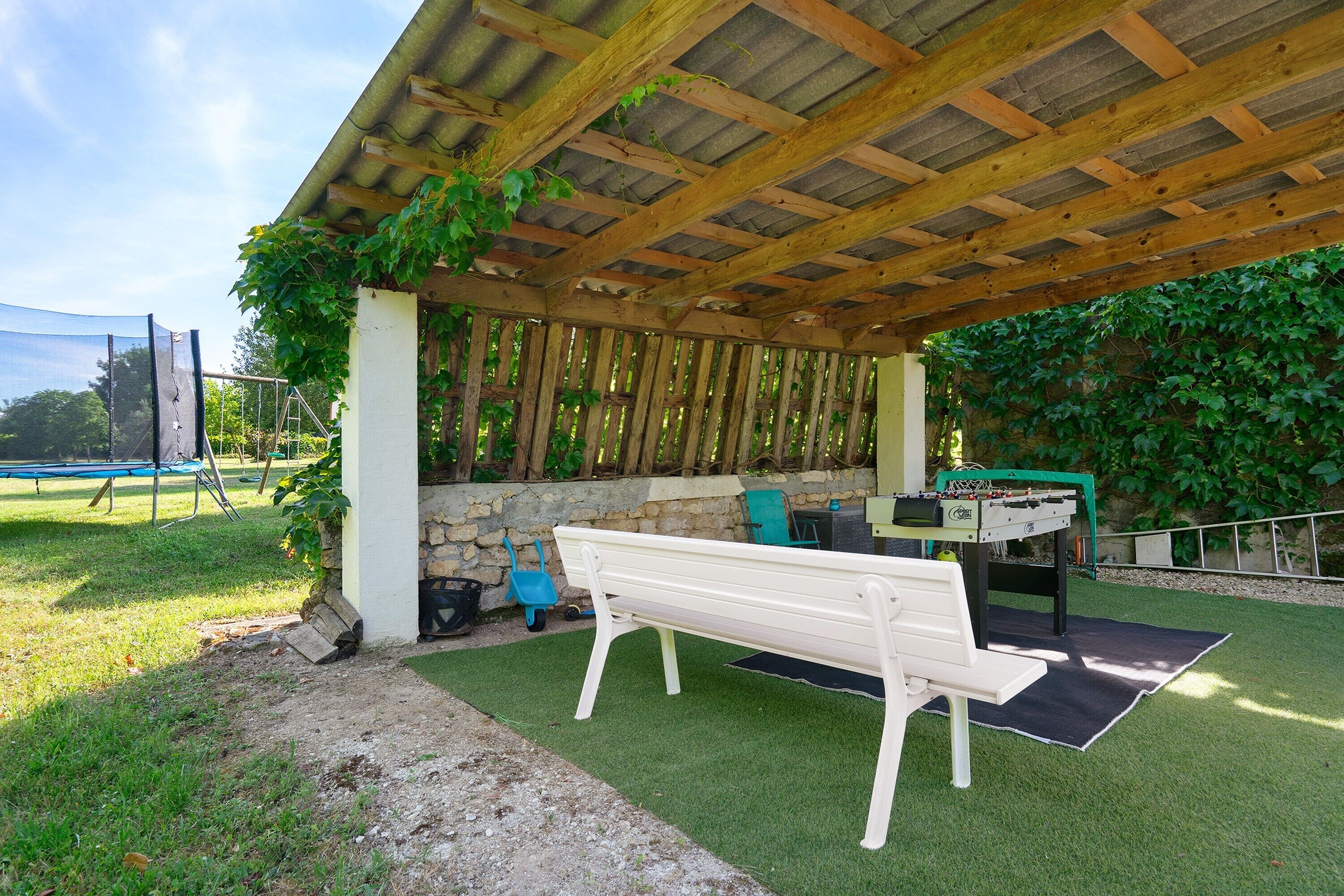 A covered outdoor area with a bench, a foosball table, and a table tennis table.