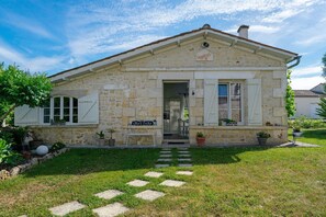 A stone building with a sign reading 'Bord de Mer,' a small bench, and a garden pathway.