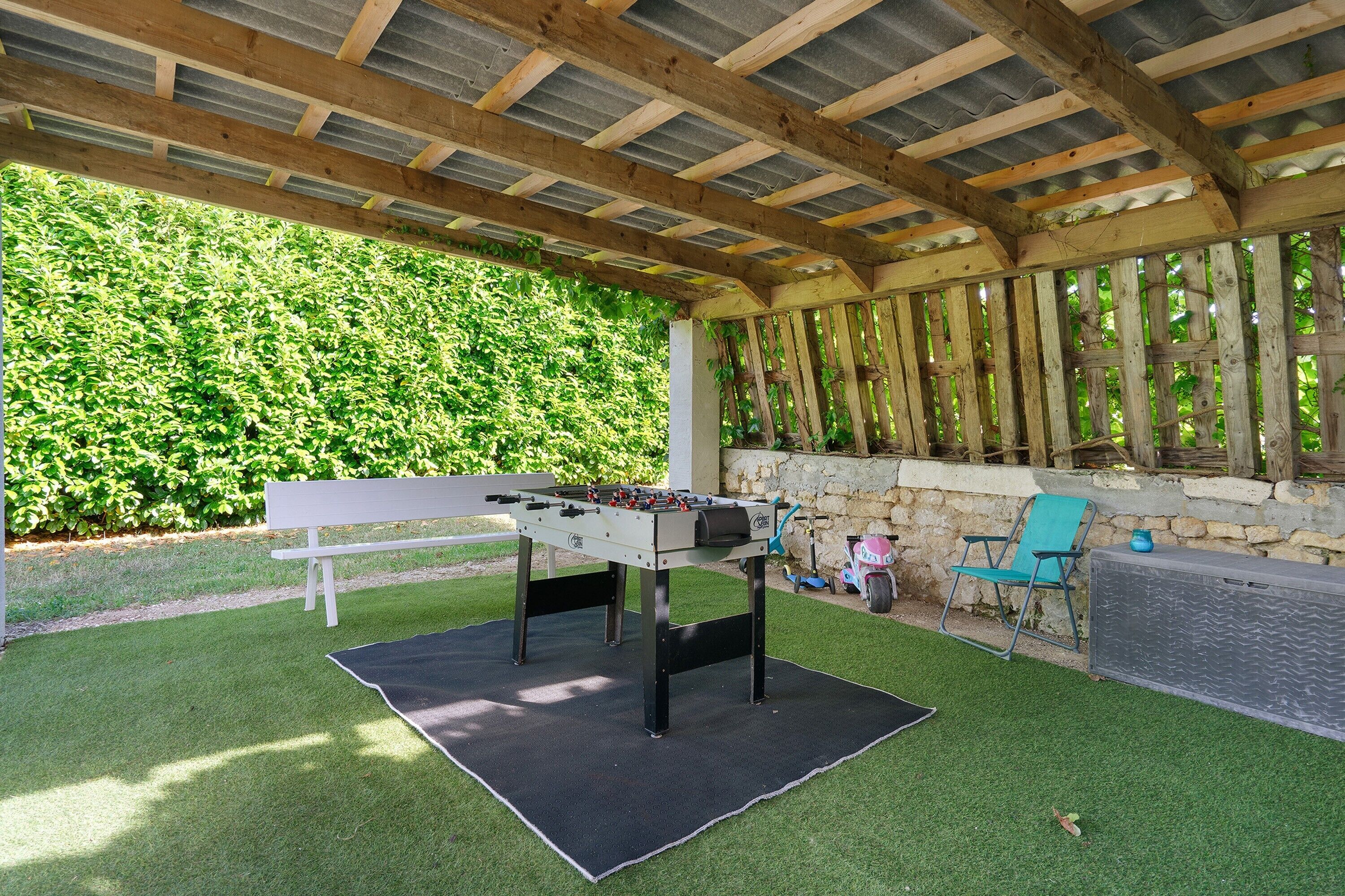 Patio esterno coperto con tavolo da calcio, una panca e un muro in pietra.