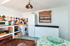 A compact kitchen with a washing machine, a refrigerator, a microwave, and a colorful diamond-patterned backsplash.