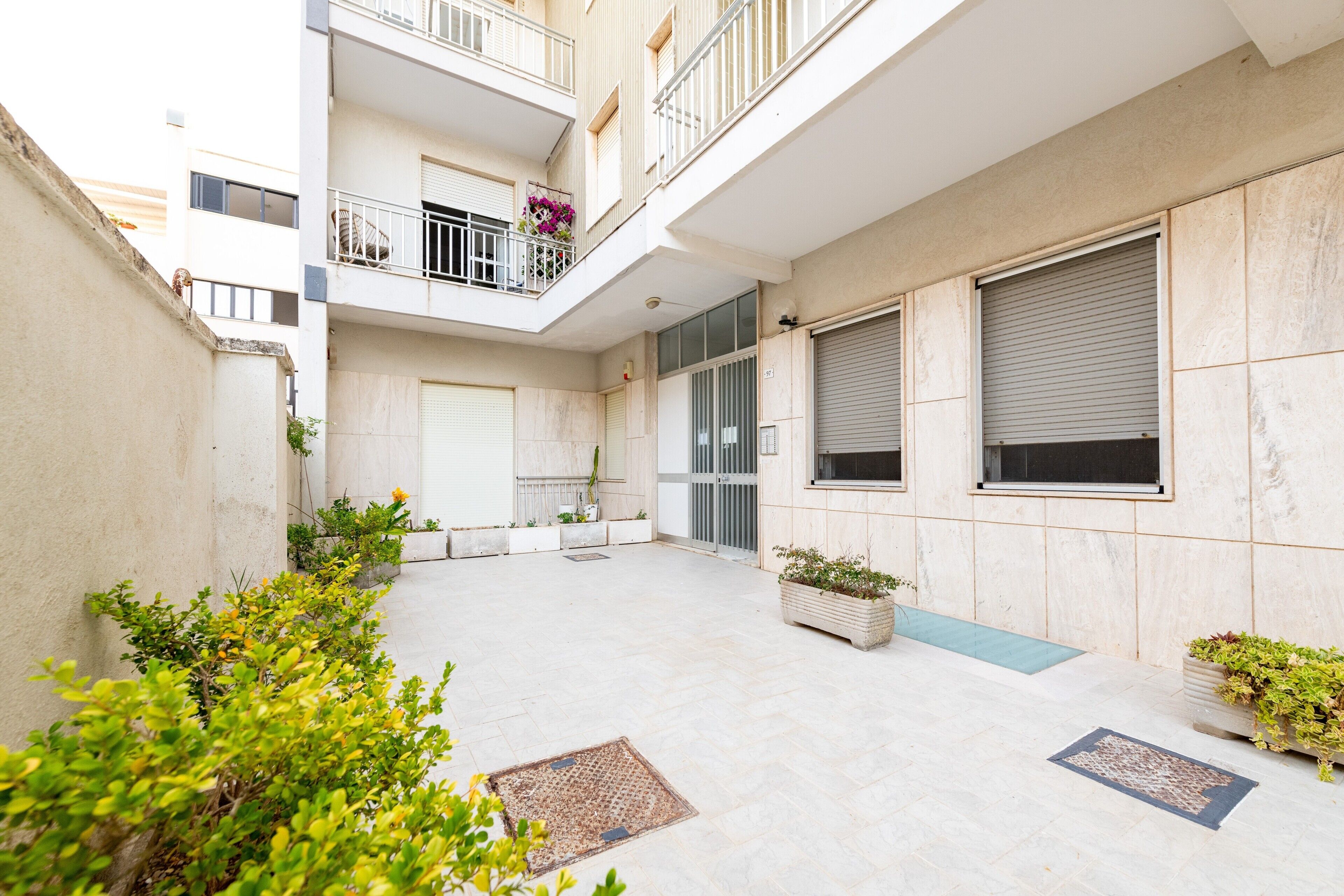 Un edificio residencial de varios niveles con balcones, entrada con portón y plantas en macetas.