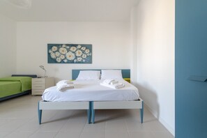 A bedroom with a bed, a bedside table, a nightstand, a green sofa, and a painting on the wall.