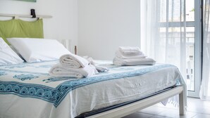 A neatly made bed with white and blue bedding, a green pillow, and a stack of white towels.
