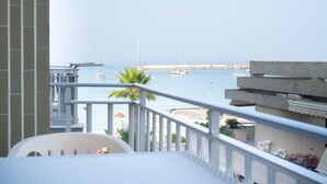 A balcony with a view of the sea, a white chair, and a small table.