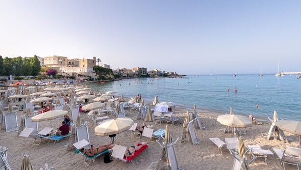 A beach with sun loungers and umbrellas, a clear sky, and boats in the water.