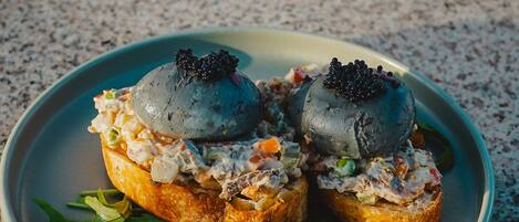 Dos sándwiches abiertos con cobertura cremosa y caviar, adornados con hojas verdes.