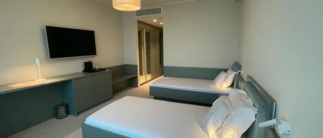 A hotel room with a bed, bedside tables, a TV, and a hanging light fixture.
