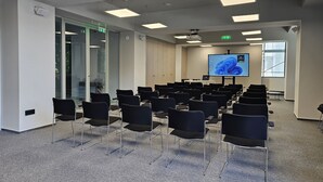 A conference room with rows of chairs, a large screen, and a door with an exit sign. - MILLENNIUM (Constanta)