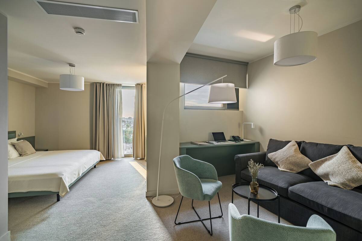 A hotel room with a bed, a desk, a sofa, and a floor lamp.