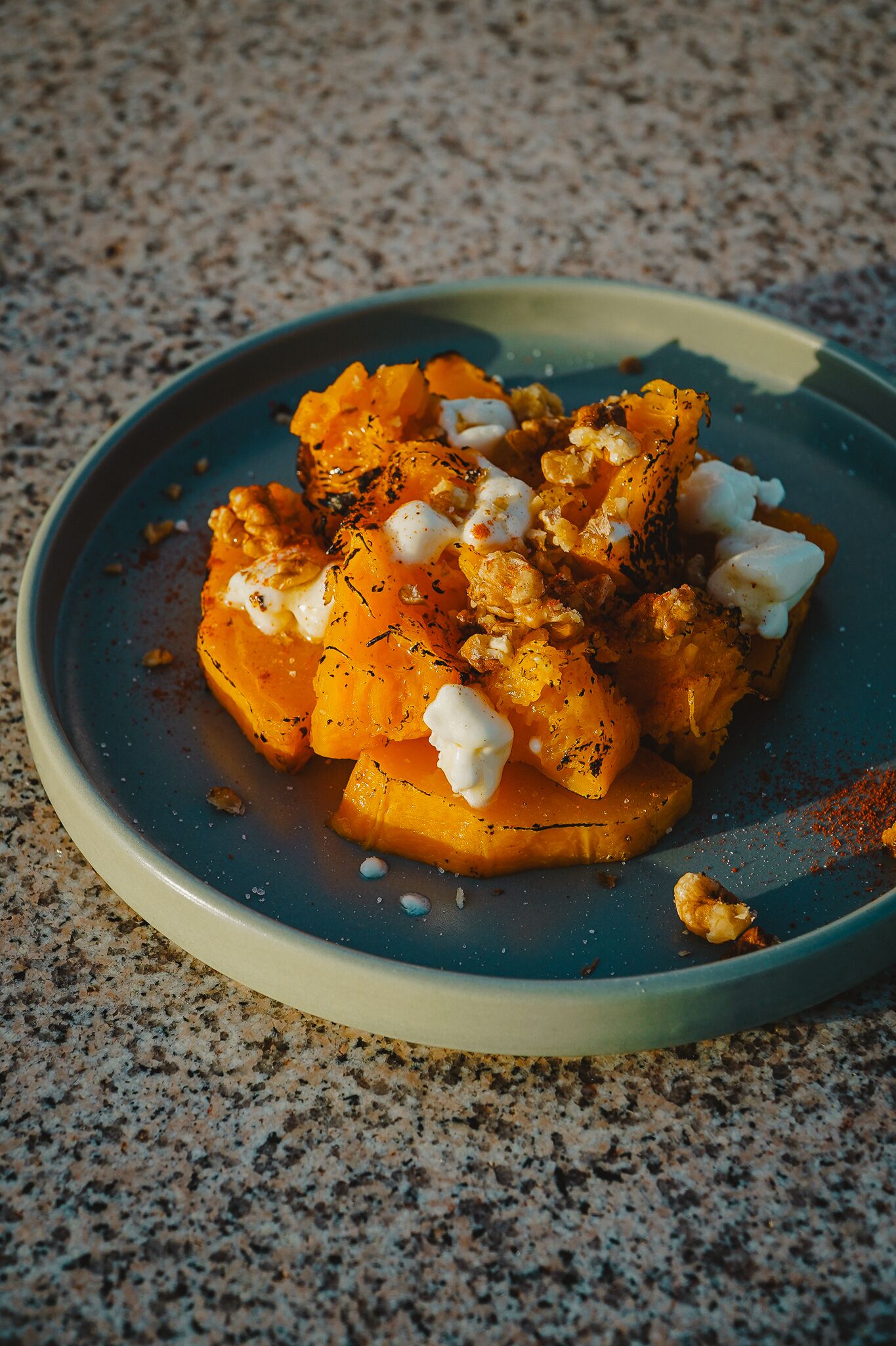 A plate of food with a blue rim, containing roasted sweet potatoes, nuts, and a dollop of cream.