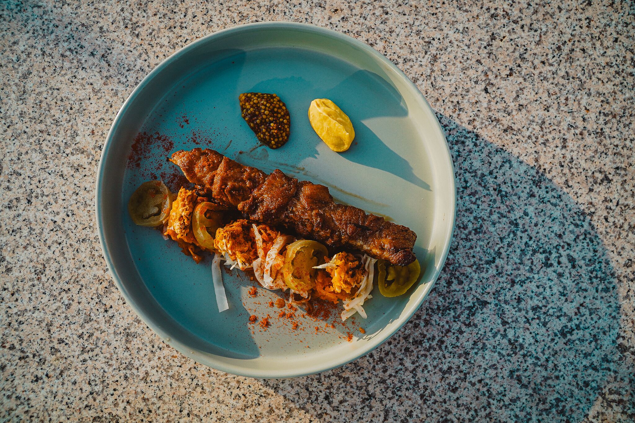 A plate with grilled meat, pickles, and a dollop of sauce on a speckled countertop.